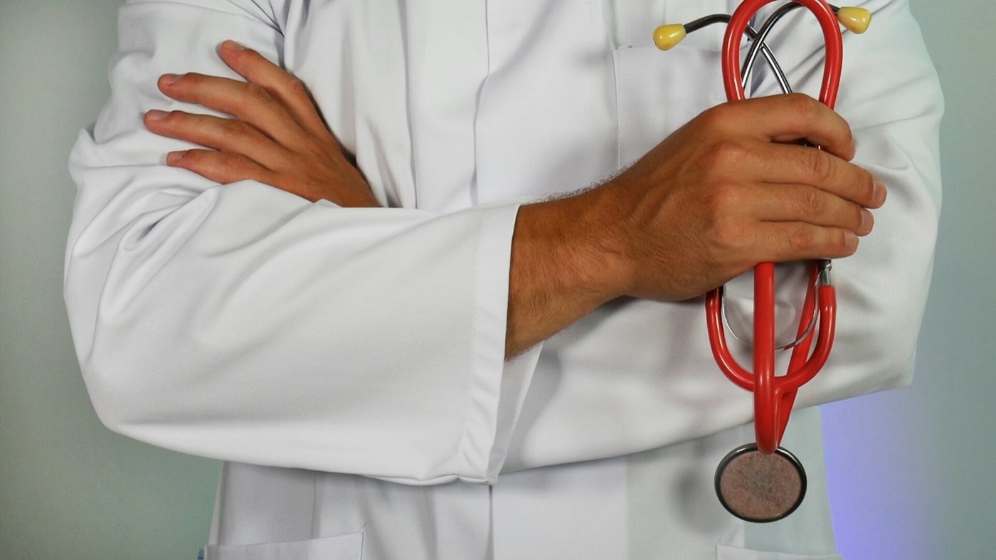 A clinician in a white coat holding a red stethoscope